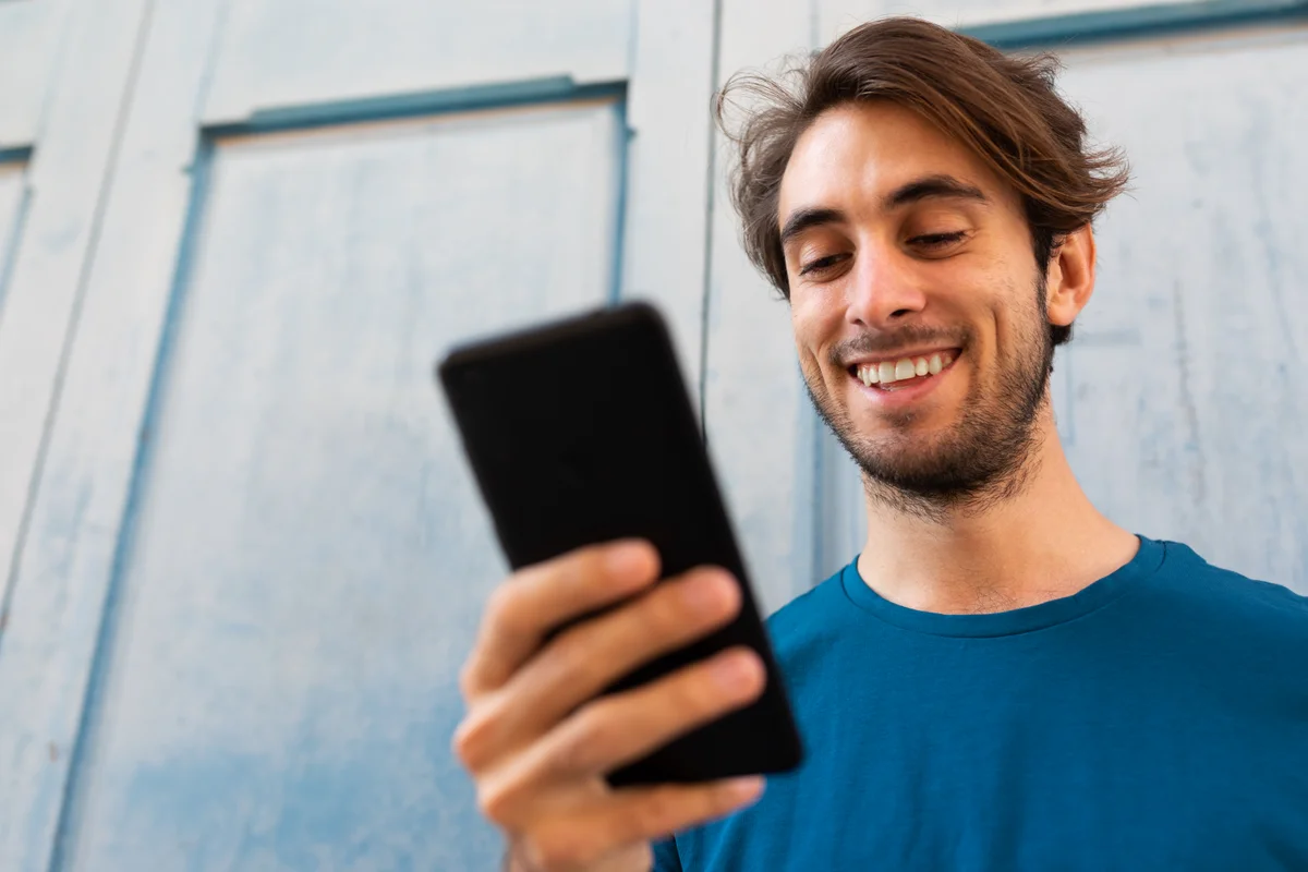 Jeune salarié souriant en consultant son téléphone, illustration de la communication CSE digitale